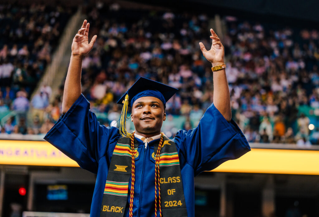 Graduate crosses UNCG commencement stage with both hands in the air.