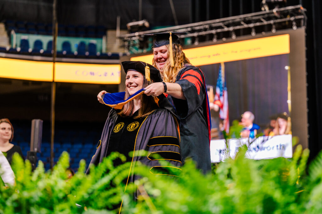 UNCG doctoral grad receives hood on the commencement stage.