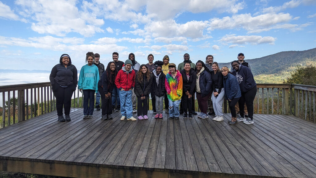 UNCG biology students stand on a wooden outlook deck with the mountains in the background.