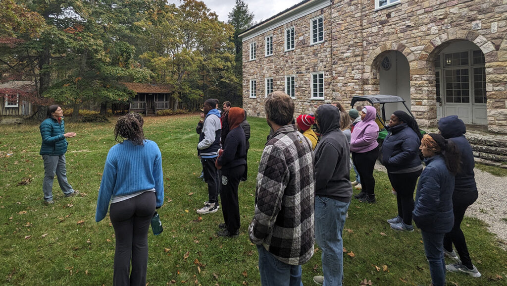 UNCG biology students listen to a speaker outside a stone building.
