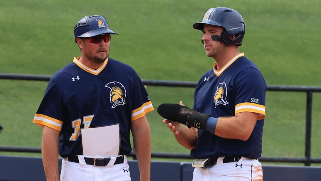 UNCG Baseball Coach Cody Ellis speaks to a player in the dugout.