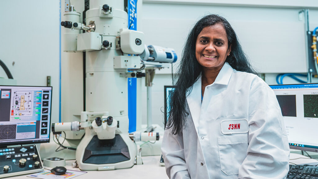 Dr. Hemali Rathnayake in her JSNN lab coat in front of a microscope machine at UNCG.