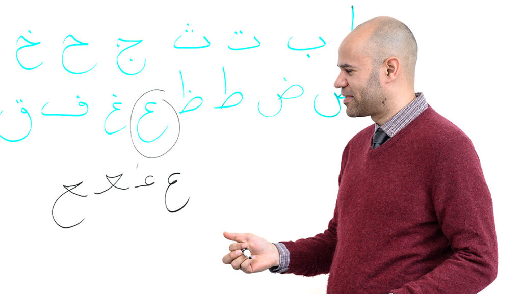UNCG psychology professor Robert Wiley in front of Arabic script written on a whiteboard.
