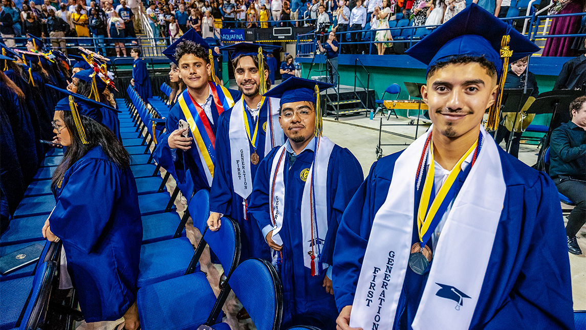 UNCG graduates in caps and gowns show off their "First Generation" stoles.