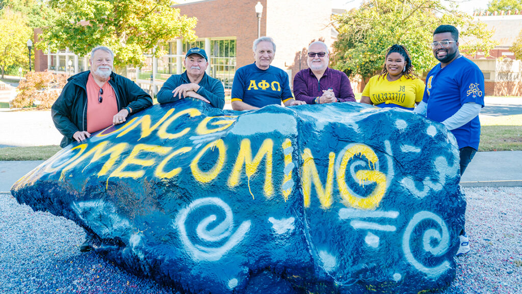 UNCG students and alumni gather around the painted Rawk on campus.