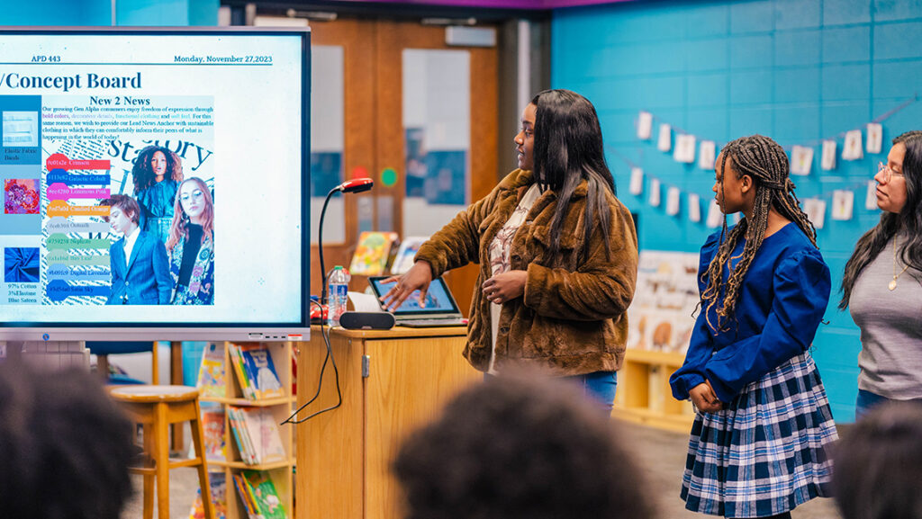 A UNCG apparel student gives a presentation while an elementary student models her new outfit.
