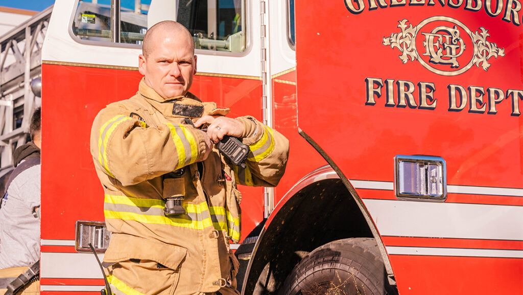 UNCG graduate Nick Loflin in his firefighting gear beside the fire truck.