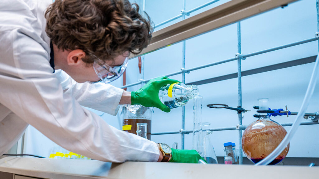 Scientist pours colorful liquid into a beaker in a lab.
