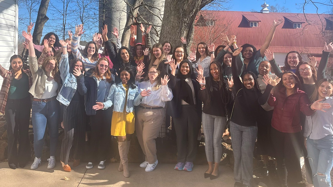 A group of healthcare students and alumni smile for a group photo outside.