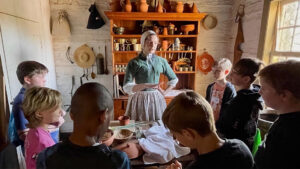 A reenactor in colonial dress speaks to a group of children.