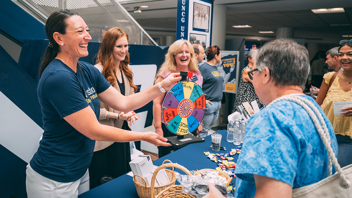 UNCG staff hold up a prize wheel for a coworker to spin.