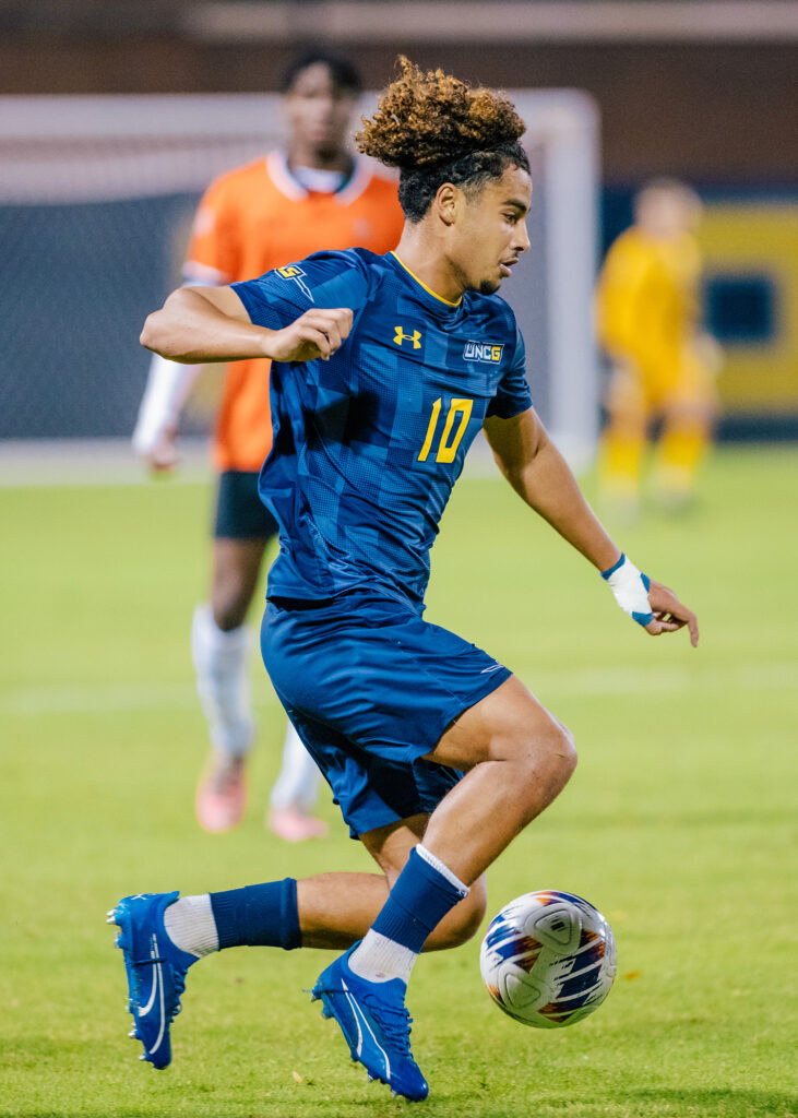 UNCG soccer player dribbles the ball down the field during a game. 