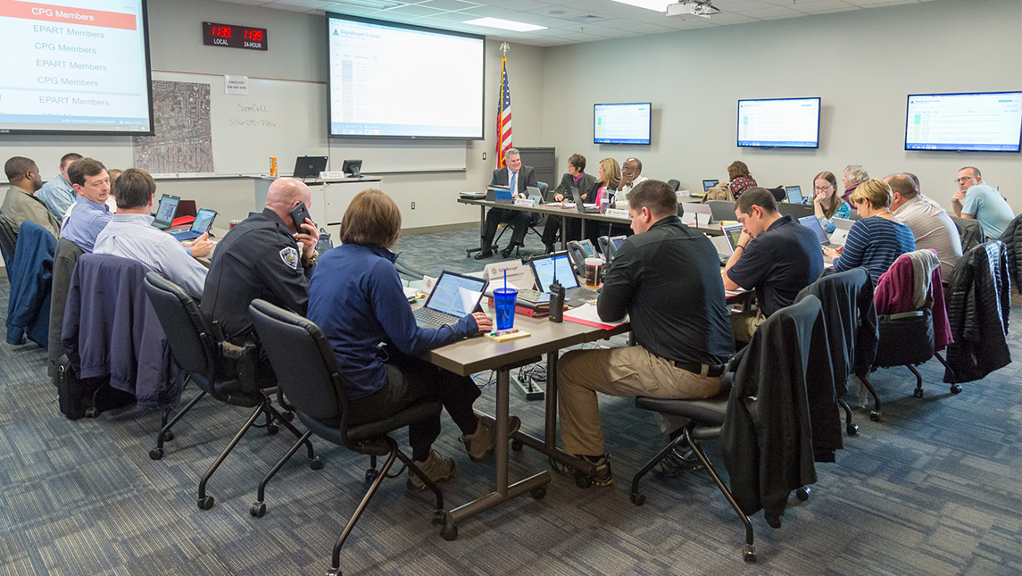 People sit around three tables with laptops.