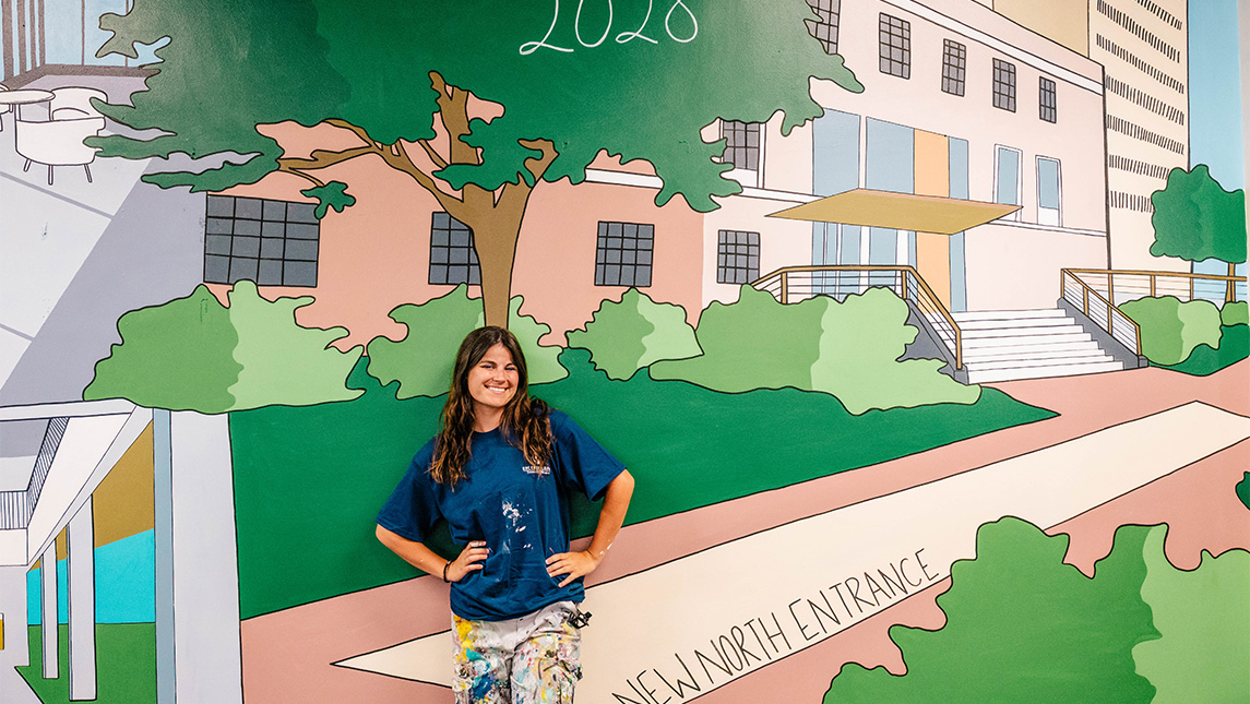 UNCG alumna Natalie Robinson '24 stands in front of the mural she painted at the library.