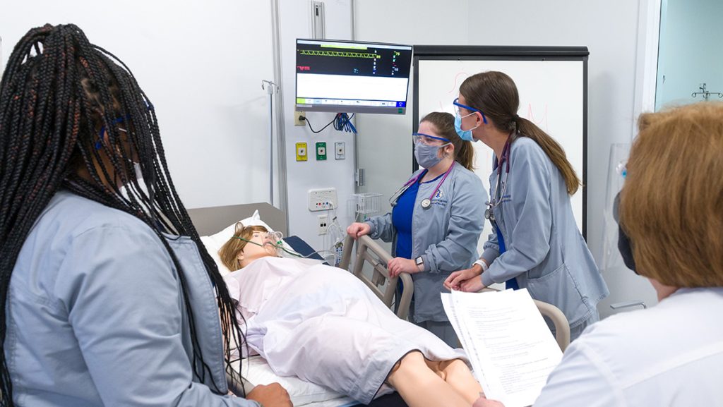 UNCG nursing students watch vitals on a display above a mannequin.