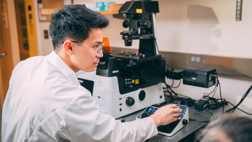 A UNCG student controls a microscope.