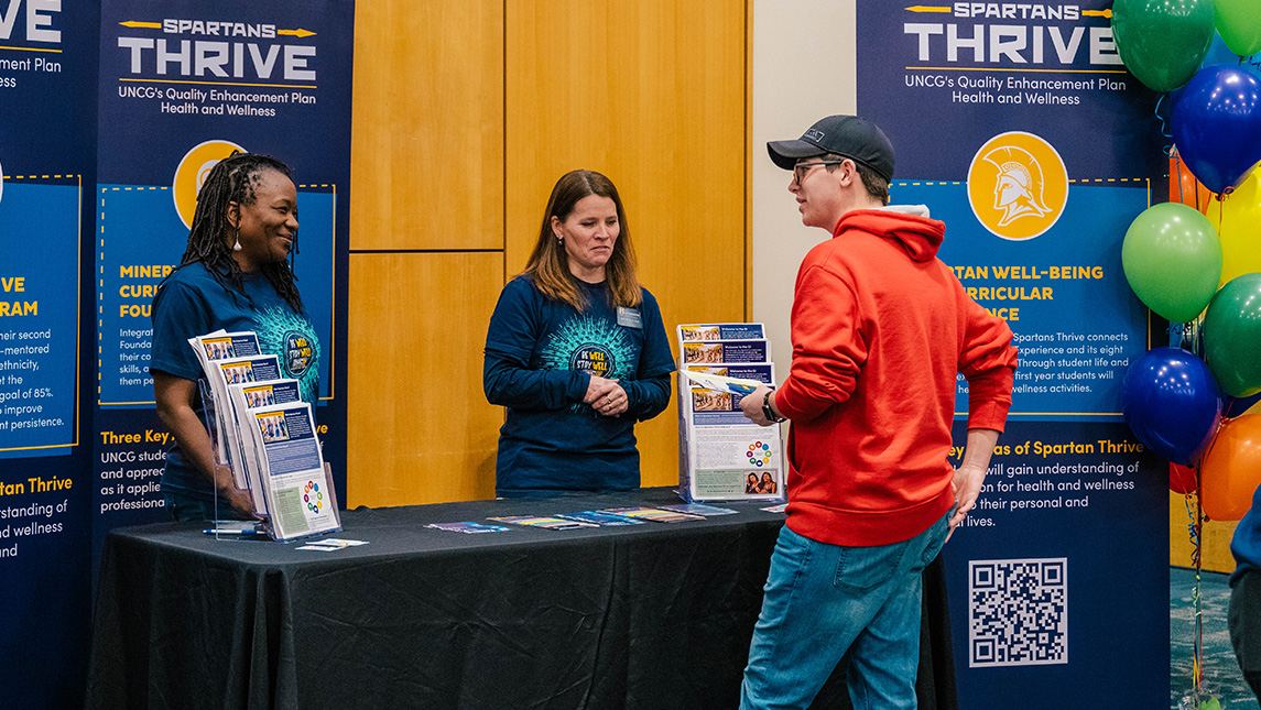 UNCG Student Success staff talk to a student beside a 