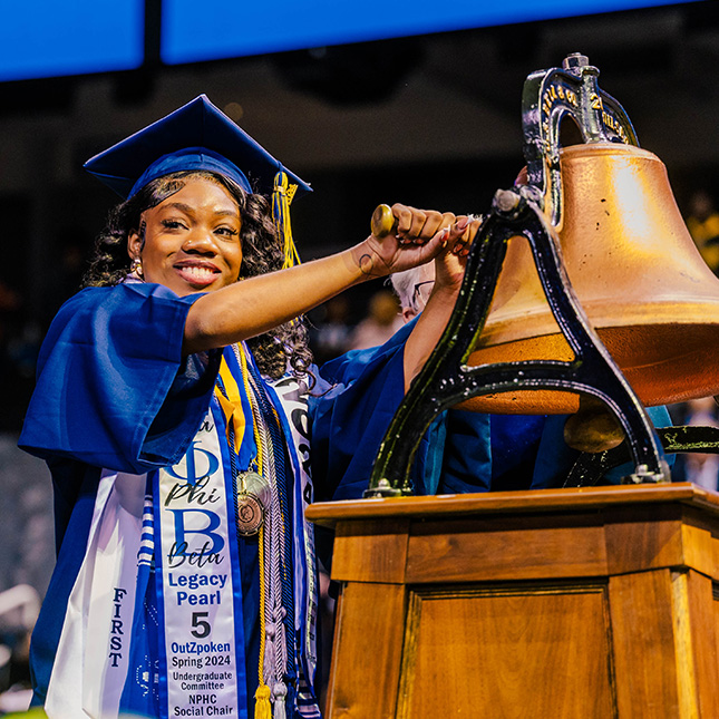 Student in cap and gown rings a bell. Student