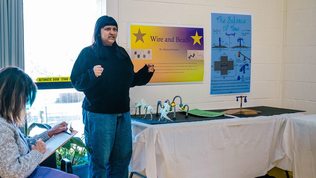 A UNCG student stands next to her model of a sculpture about movement.