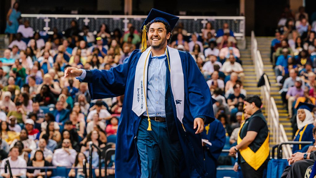 A UNCG college graduate crosses the stage at Commencement wearing a first generation stole.