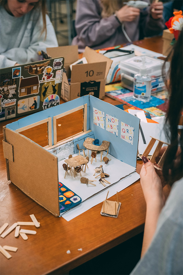 A UNCG student adds miniature props to her cardboard model of a classroom.