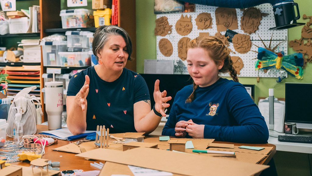 School of Education Professor Sara Porter talks to a student while she cuts cardboard.