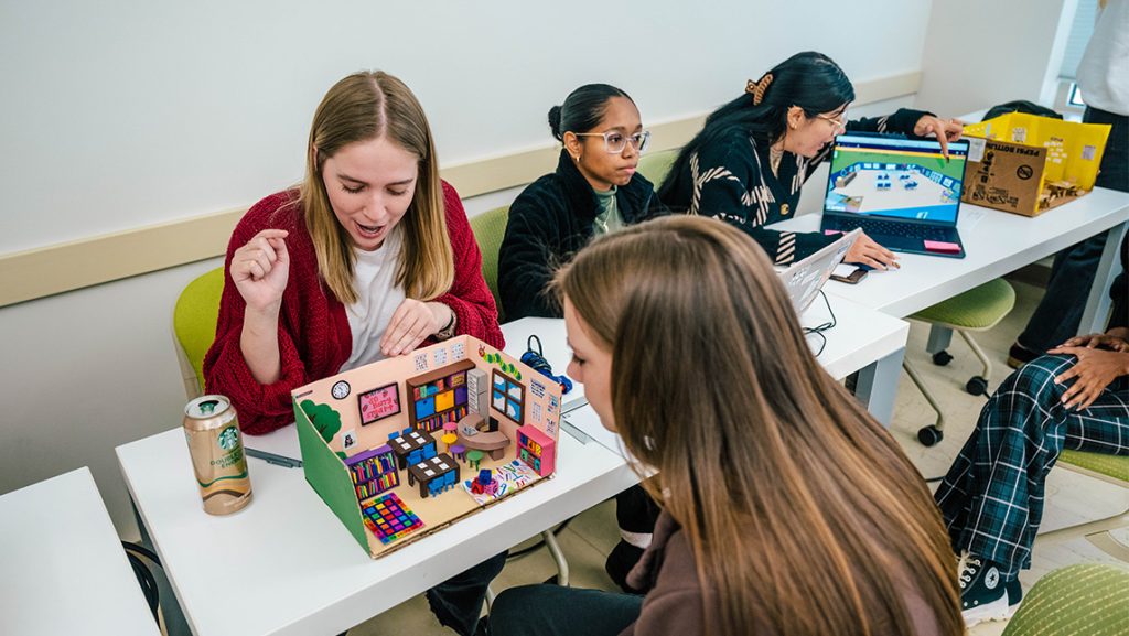 A UNCG student explains to her classmates what she put inside her cardboard model of a classroom.