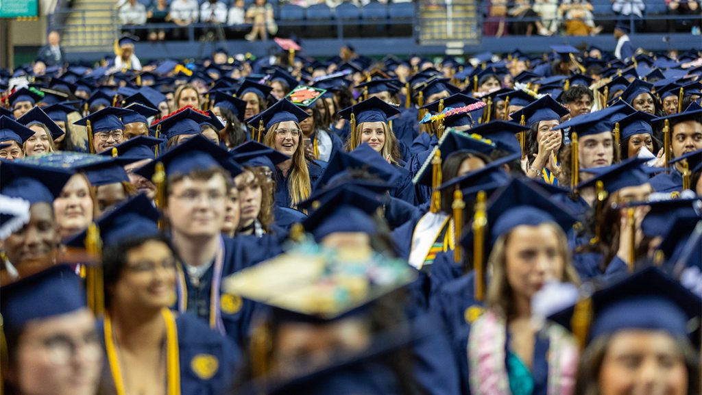 A crowd of UNCG students graduating in their caps and gowns.