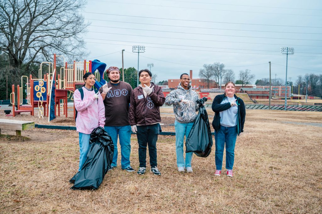 A group of students at a school playground hold lawn debris trash bags.