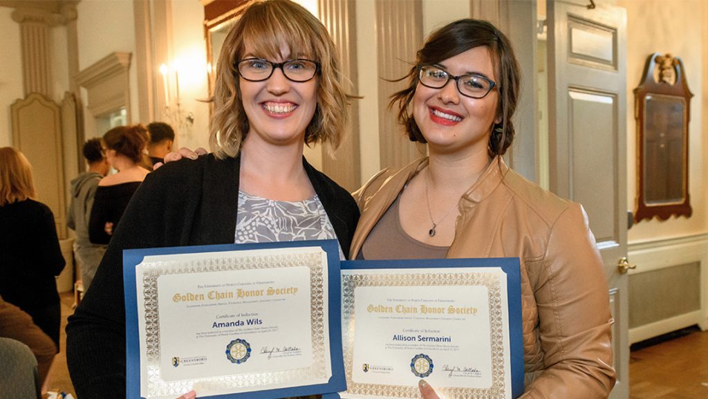 Two UNCG students hold up their Golden Chain Society certificates.