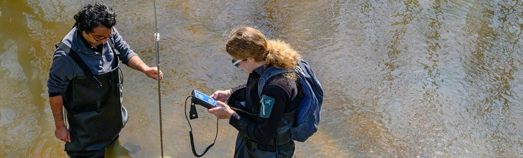Faculty and student take measurements in creek bed