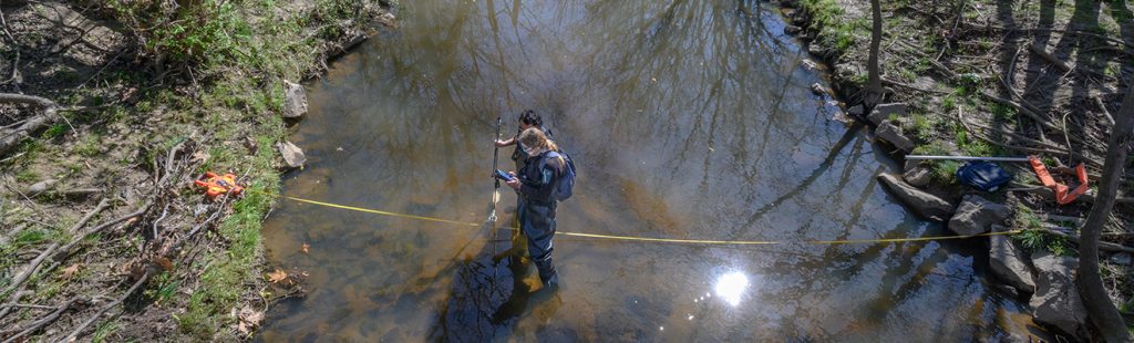 Faculty and student take measurements in creek bed