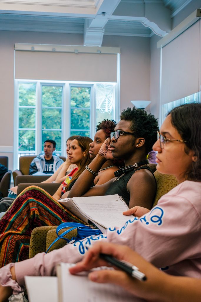 A group of students sitting in couches and chairs looking toward a speaker.