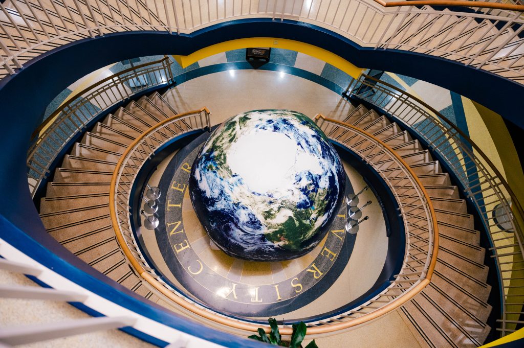 An overhead view of a globe sculpture at the bottom of two-sided staircase.