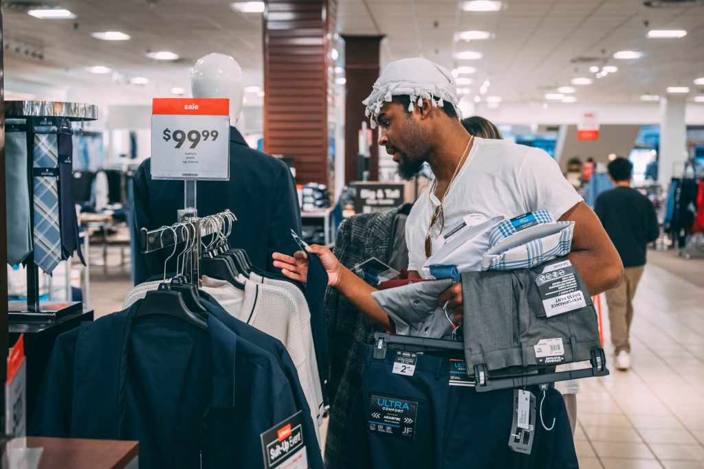 Student looks through racks at JCPenney with an armful of pants and shirts.