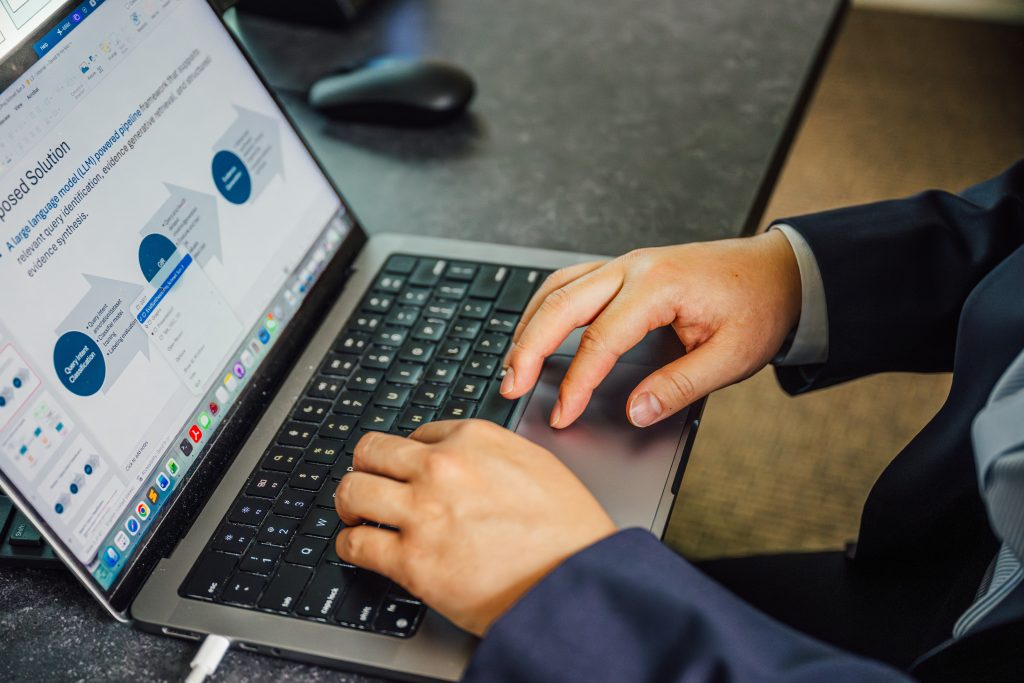 A closeup shot of hands resting on a laptop keyboard. The laptop screen shows a presentation with data flowchart.