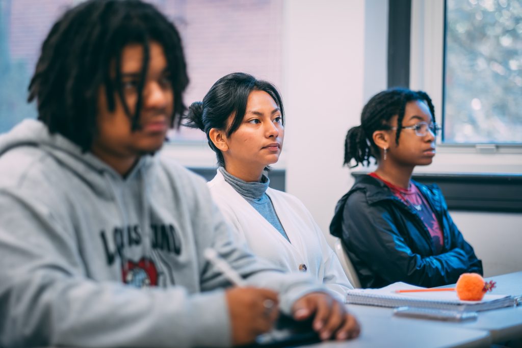 Three students sitting at a desk in a classroom setting.