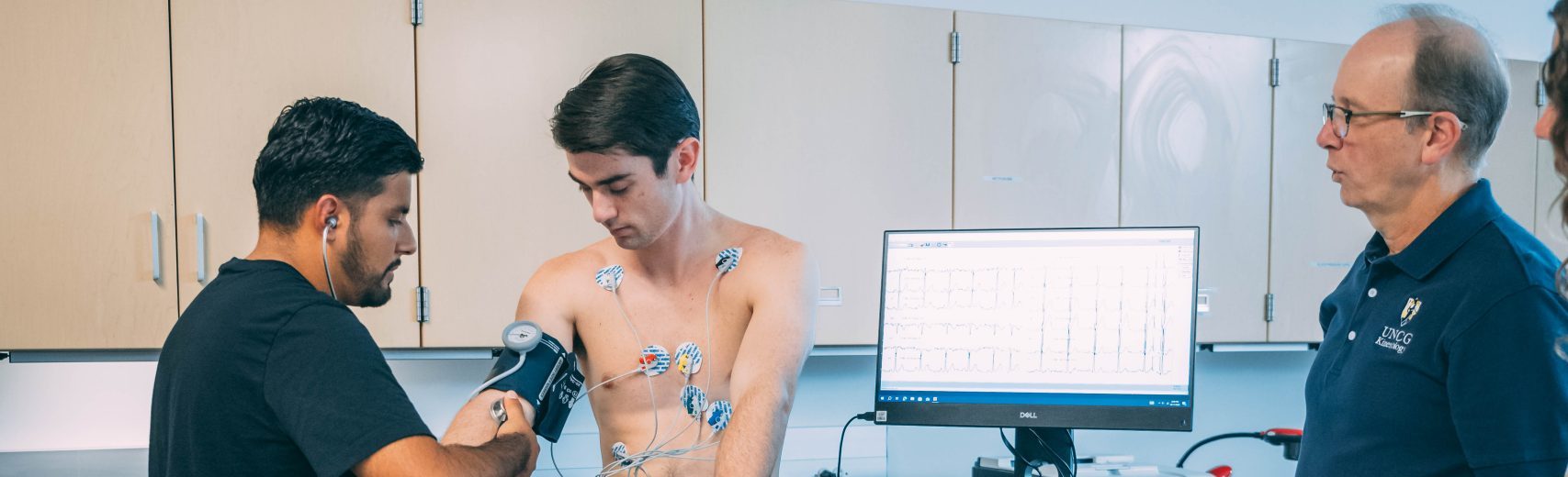A student takes vitals on another student while a professor watches.