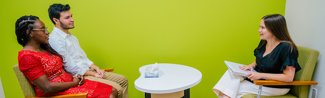 A couple sits across a table from another person who holds a notebook.