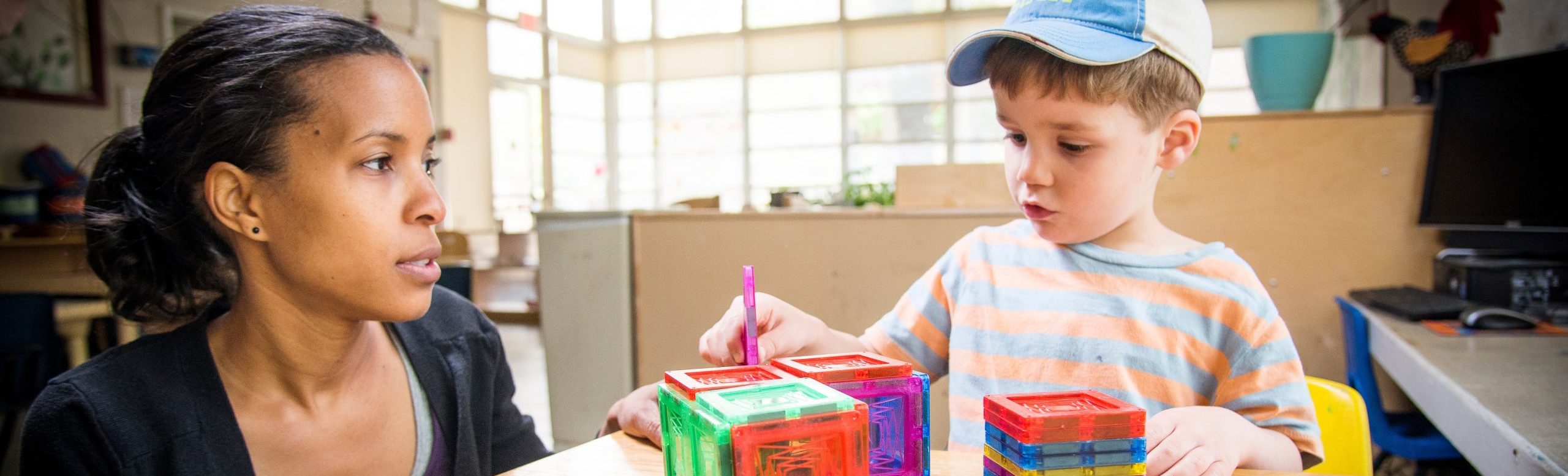 Woman works with magnetic tiles with a child.