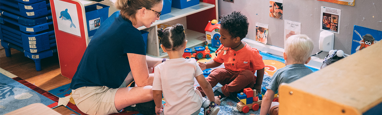 A woman plays with three toddlers in a daycare.