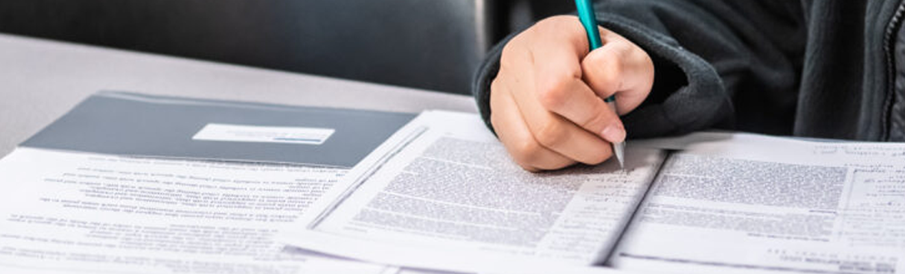 A hand holding a pen makes notes in the margins of printed reading.