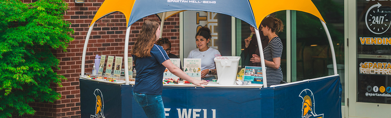UNCG students stand in an outside booth talking to a passerby.