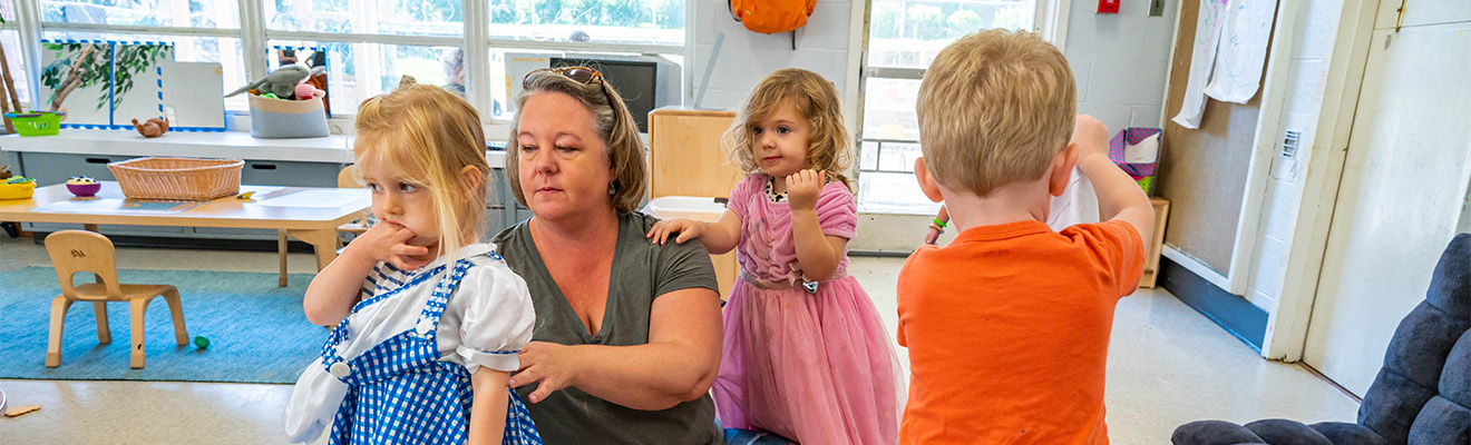 A woman helps children put on dress-up clothes.