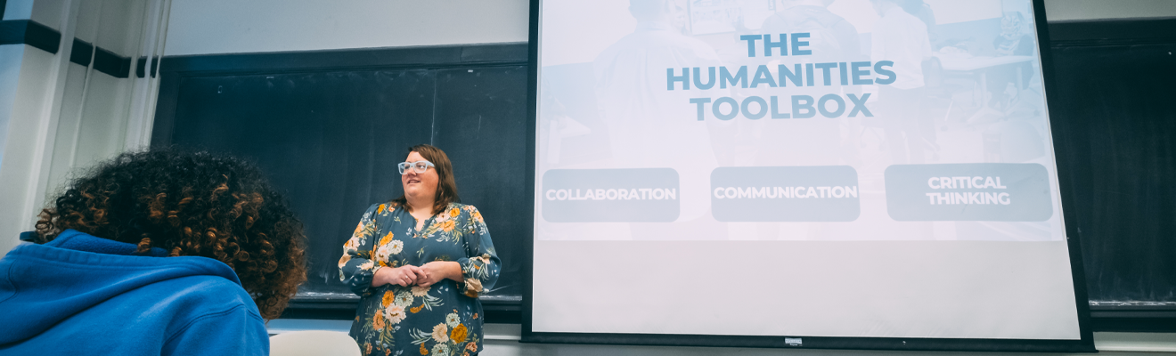 An instruction standing in front of a classroom presenting a slide entitled "The Humanities Toolbox."