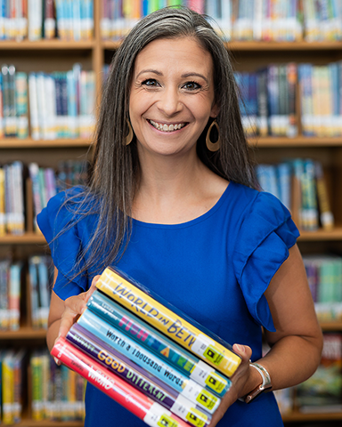 MLIS alum Jen Miller holds a stack of books while standing in a library
