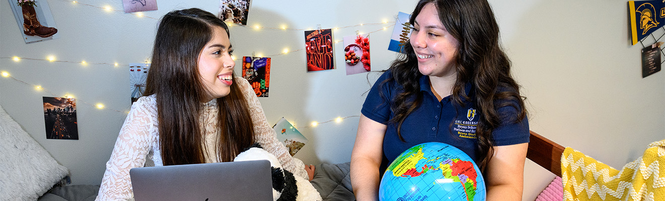 Two students, one working on a laptop while the second holds an inflatable globe.