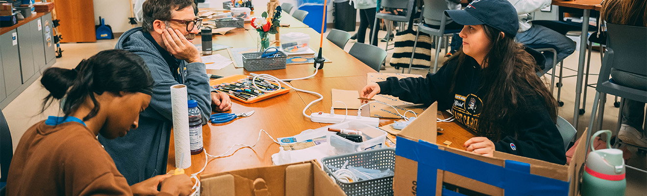 Students sit around a table cutting cardboard in the UNCG makerspace.
