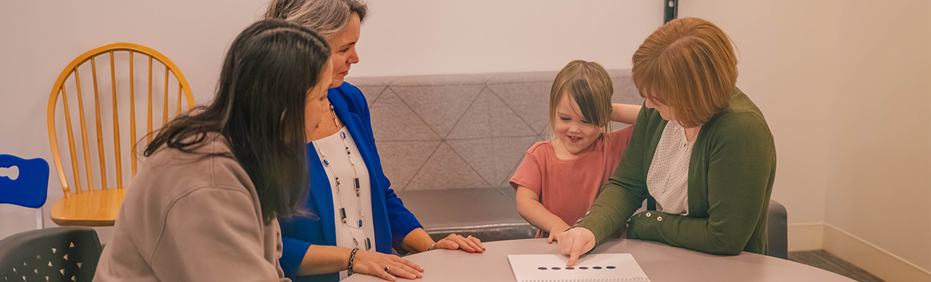 Three adults work with a child at a table with papers.