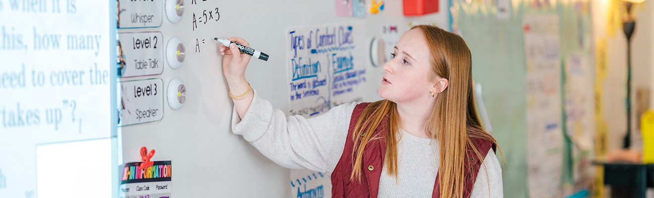 A UNCG student teacher writes math equations on a whiteboard.